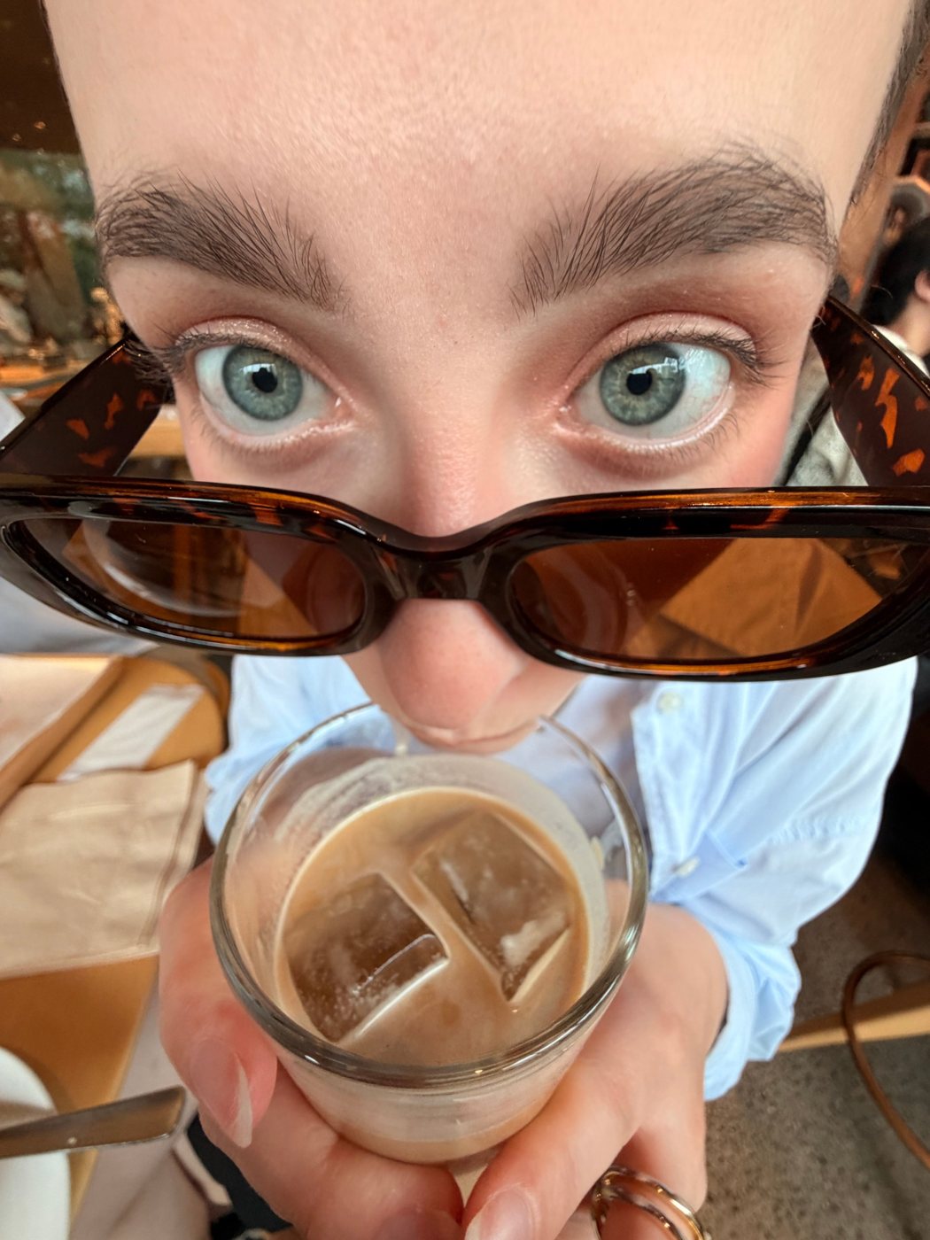 Nati olhando por cima dos óculos de sol enquanto toma um café gelado